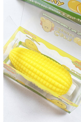 A yellow corn-shaped stress ball inside a clear plastic blister pack with printed packaging, photographed on a plain light background.