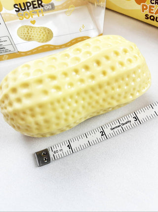 A yellow corn-shaped squishy toy with a textured pebble pattern, shown next to a tape measure and its packaging on a white surface.