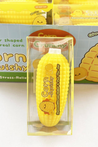 A yellow corn-shaped squishy stress relief toy in a clear plastic blister pack, with its branded packaging box visible in the background.