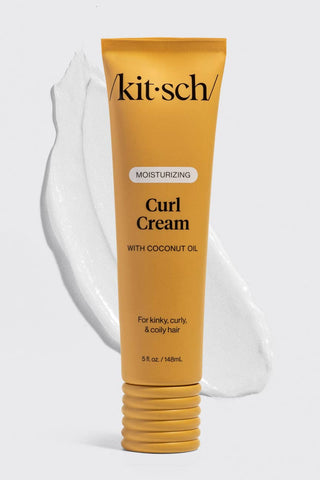 A tube of Kit Sch Curl Cream with coconut oil, shown in a golden yellow color with a white cream smear behind it on a light gray background.
