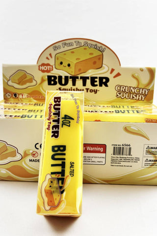 A yellow 4 oz stick of Butter Crunchy Squishy Salted Quishu Toy, standing in front of its matching yellow and cream packaging display box.