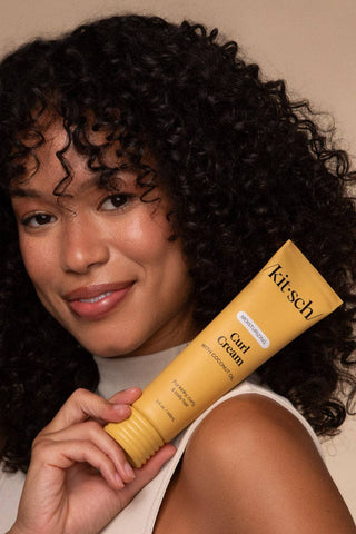 Woman holding a yellow tube of 'kitsch' hair product against a beige background