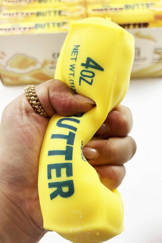 A hand squeezing a bright yellow butter wrapper that has '4oz BUTTER NET WT' printed on it, with a blurred butter box in the background.