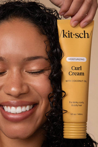 Person holding a tube of 'kitsch' Curl Cream with coconut oil against a beige background