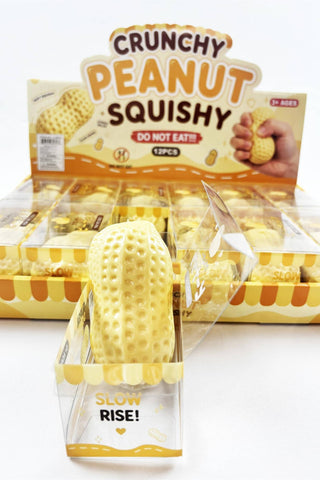 A display box of Crunchy Peanut Squishy novelty snacks, featuring a large yellow peanut-shaped squishy in the foreground and multiple smaller ones inside a clear plastic display tray. The packaging is yellow and white with bold text reading 'CRUNCHY PEANUT SQUISHY' and 'DO NOT EAT!!!'.