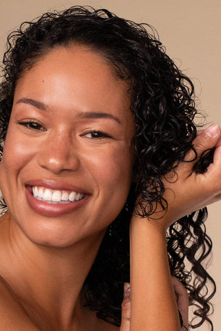 Woman with curly hair smiling against a beige background