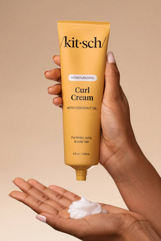 Hand holding a tube of 'kitsch' Curl Cream with coconut oil against a beige background