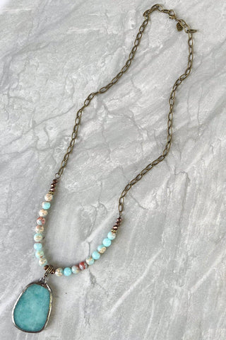 Amazonite stone beaded necklace with natural stone pendant and bronze chain on white marble surface.