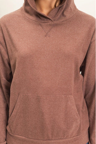 A close-up of a person wearing a heathered dusty rose brown pullover hoodie with a front kangaroo pocket and a split neckline.