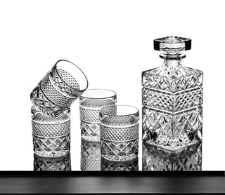 Set of crystal glasses and a decanter on a reflective surface with a white background