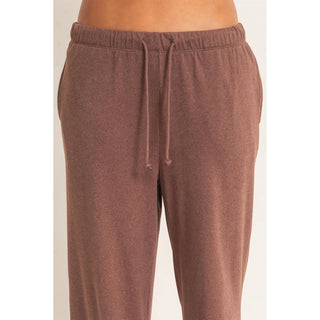 A close-up of a person wearing heathered brown drawstring sweatpants against a plain light background.