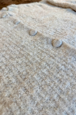 Close-up of a cream-colored textured knit garment with large round buttons, showing the fuzzy wool-like fabric detail.