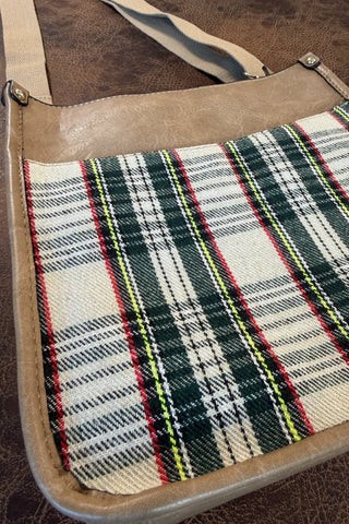 A close-up of a shoulder bag featuring a tan faux-leather trim and strap, with a front panel made of a green, black, white, and red plaid woven fabric.