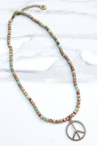 Necklace with multicolored beads and a peace symbol pendant on a marble surface