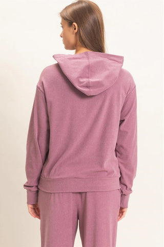 A woman shown from the back wearing a dusty rose pink hooded sweatshirt and matching sweatpants against a plain off-white background.