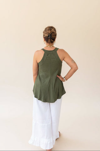 Person wearing an olive green sleeveless top and white pants on a beige background