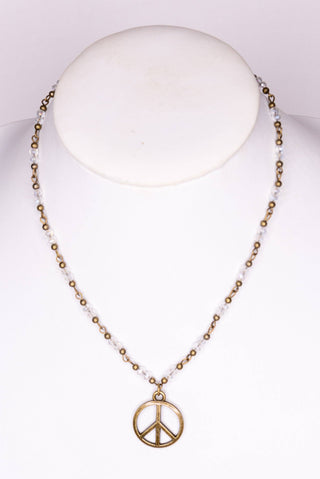 Gold beaded peace sign necklace with clear crystal beads and bronze pendant on blush marble surface
