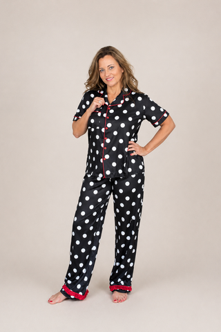 Woman wearing black polka dot pajamas with red trim on a beige background