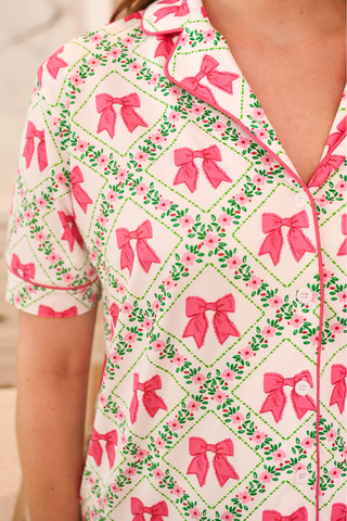 Close-up of a patterned shirt with pink bows and green leaves on a white background