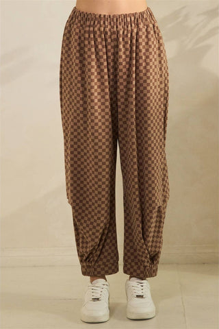 Brown and beige checkered harem pants with an elastic waist and ankle cuffs, shown on a model wearing white sneakers against a neutral beige background.