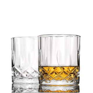 Two clear glass tumblers with one containing a yellow liquid on a white background