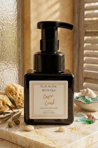 Ellie & Oak Boutique Capri Coast Handmade Soap in a black pump bottle, styled on a marble tray with seashells and dried botanicals against a warm beige background.