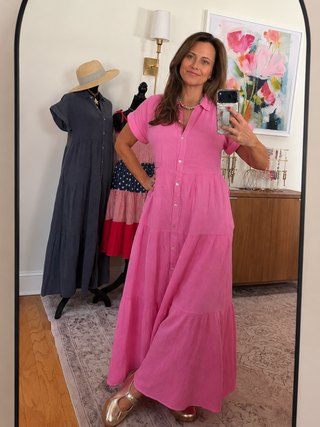 Woman taking a mirror selfie wearing a pink dress in a room with clothing racks and decor.