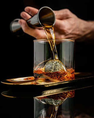 Hand pouring whiskey into a glass with a dark background