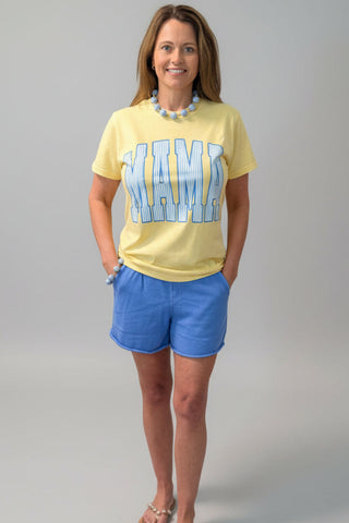 Woman wearing a yellow t-shirt with blue mama and blue shorts on a gray background
