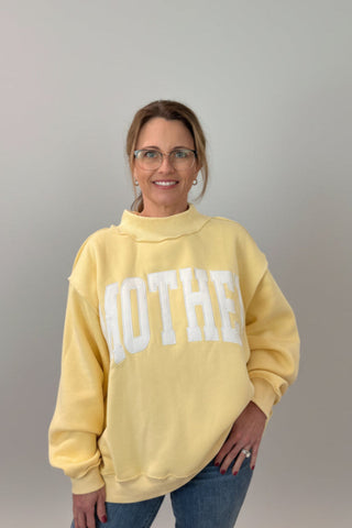 Woman wearing a yellow sweatshirt with embroidered mother text.